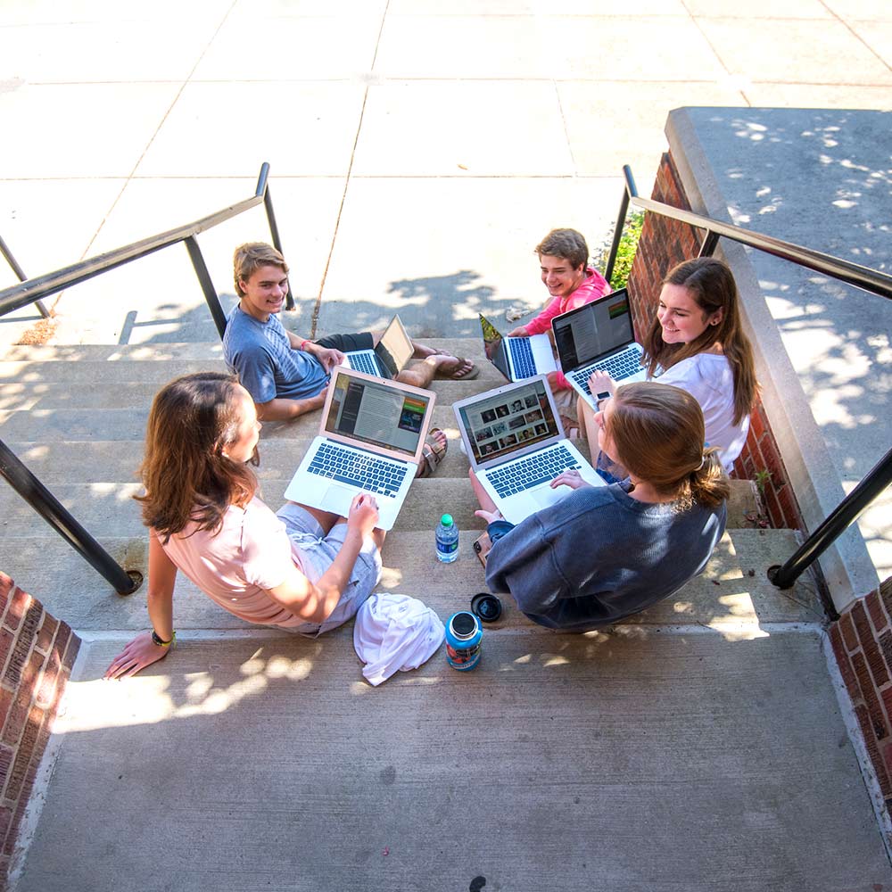 Group of high school seniors sitting outside on steps with laptops